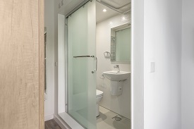 An en suite in Old Vicarage. The en suite door is open which shows the toilet and a towel rail above the toilet. Outside of the en suite is a bed with a television mounted on the wall.